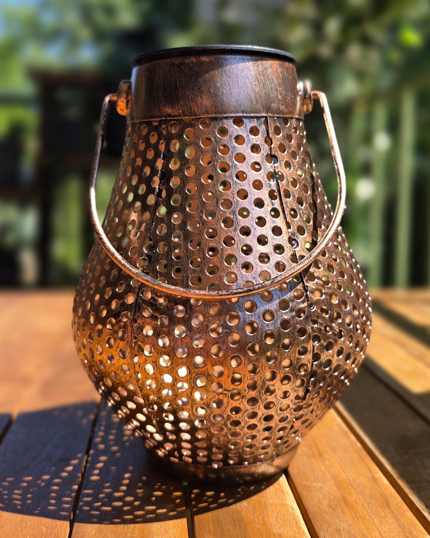 Lanterne solaire DOTY Lumisky vue de trois quarts, finition métal cuivré vieilli aux reflets dorés, fond de terrasse en bois ensoleillée