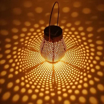 Lanterne solaire DOTY Lumisky allumée de nuit, métal perforé finition cuivrée vieillie, jeux d'ombres chaleureux, lumière LED blanc chaud, terrasse extérieure