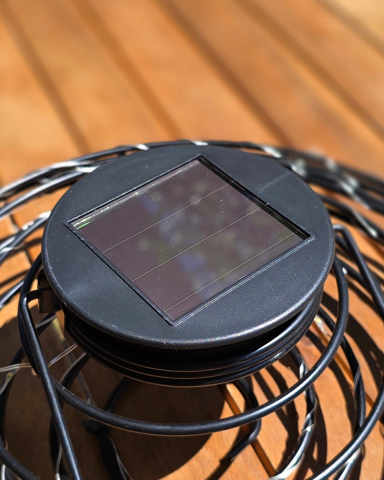 Détail panneau solaire intégré au sommet de la suspension ORION Lumisky, couvercle noir rond avec cellule photovoltaïque carrée, posé sur table en bois