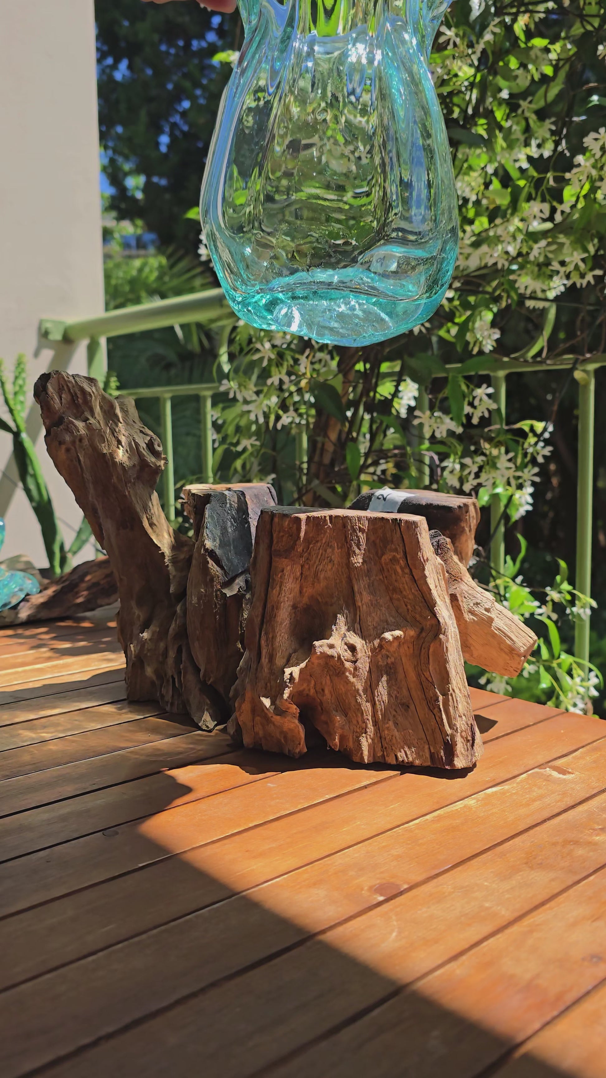 Vidéo — Gros plan du grand vase à lèvres LaPailleBambou en verre soufflé recyclé sur socle en teck, présenté sur une table en bois au soleil, reflets aqua translucides — LLX ConceptStore
