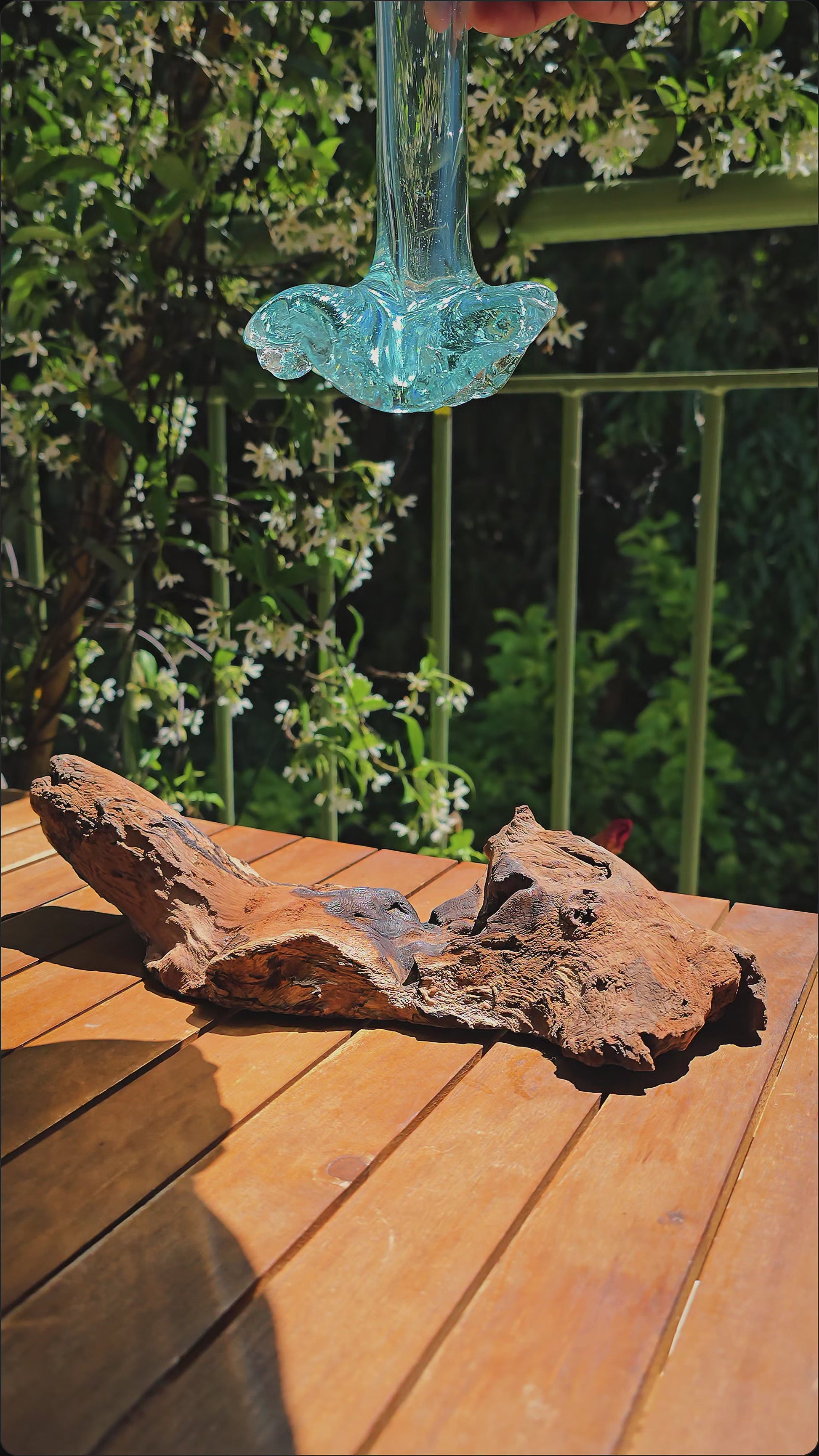 Vidéo — Gros plan du soliflore artisanal LaPailleBambou en verre soufflé recyclé sur socle en teck, posé sur une table en bois au soleil, reflets aqua translucides — LLX ConceptStore
