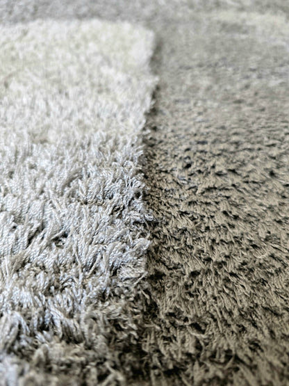Détail de la texture sensorielle des poils longs et denses d'un tapis cocooning gris haute qualité.